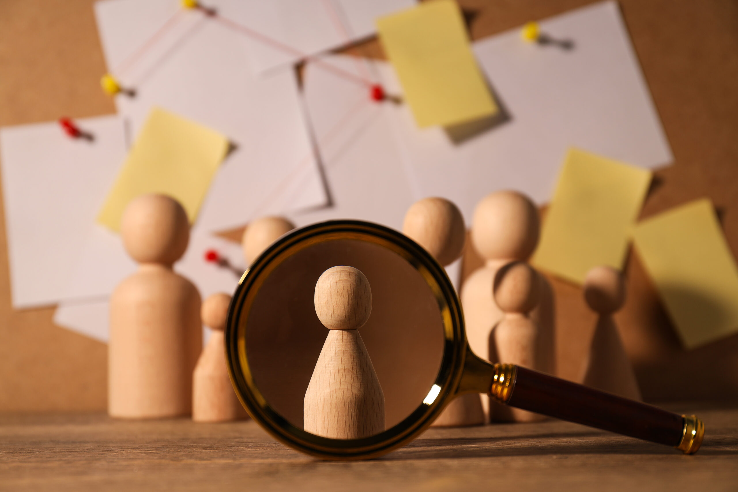 Magnifying glass focusing on a wooden figure among a group, symbolizing Intrinsic HR’s neutral, expert, and confidential approach to workplace investigations.
