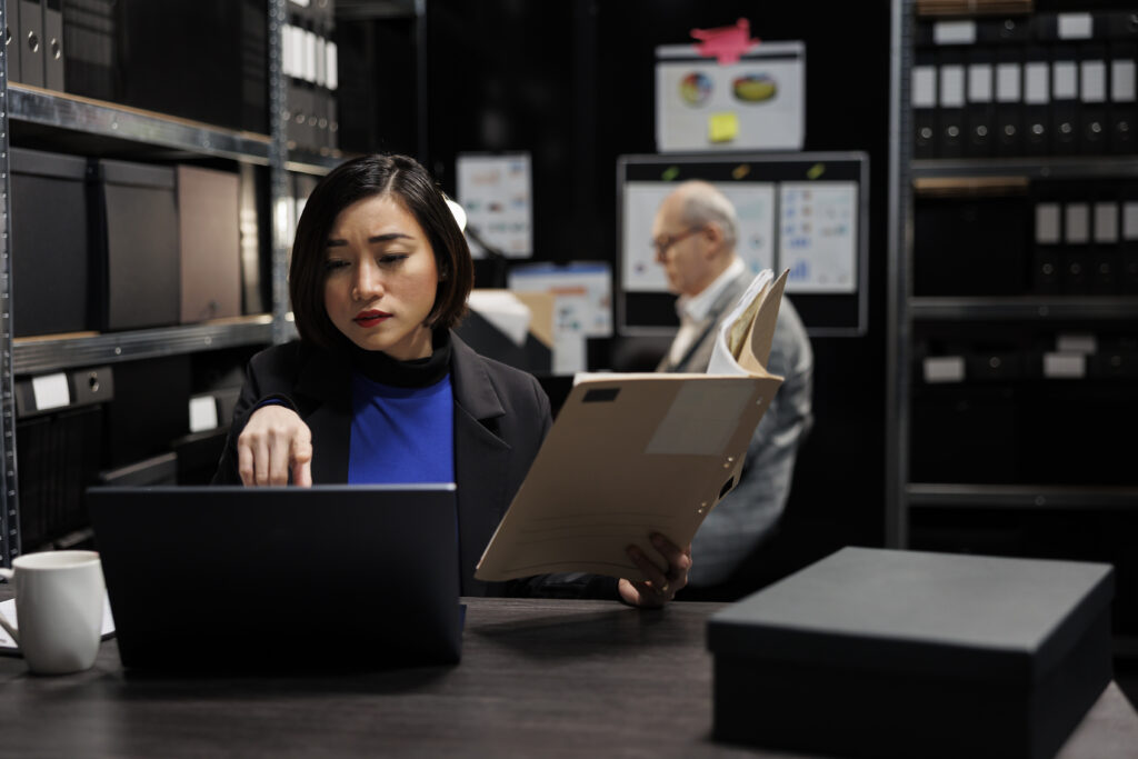 Professional reviewing documents and working on a laptop in a storage room, symbolizing how HR tasks can overwhelm internal teams as a business and workforce grow.