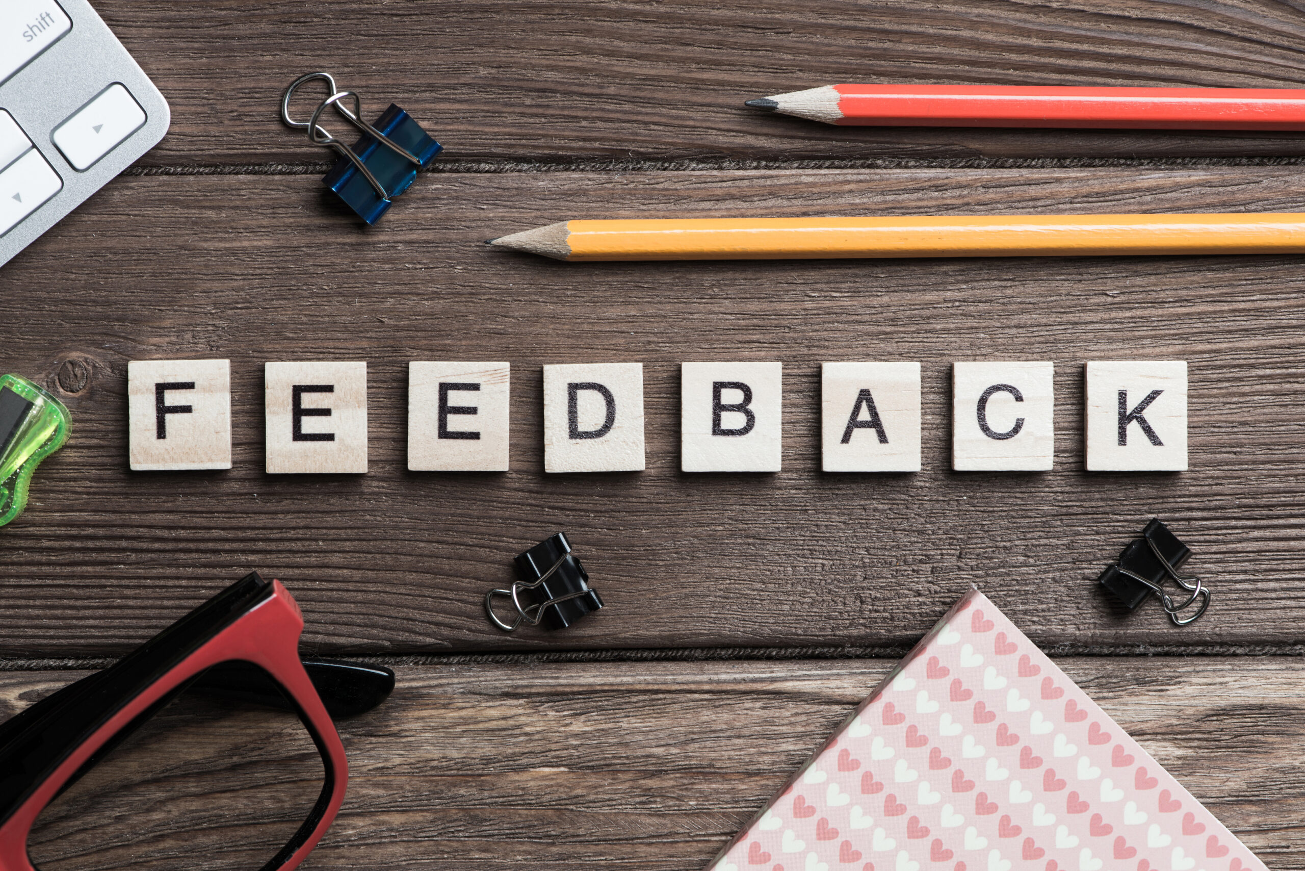 Wooden tiles spelling “Feedback” surrounded by office supplies, symbolizing transforming performance reviews from basic paperwork into strategic tools for growth and engagement.