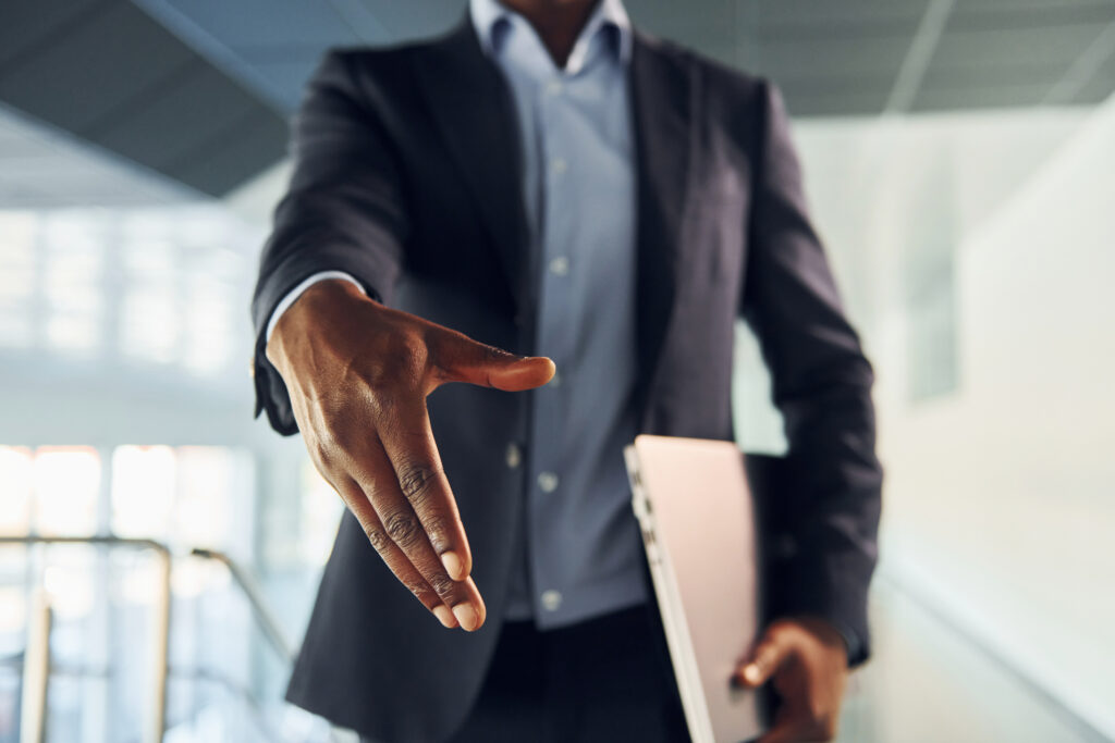 Business professional extending a hand for a partnership, symbolizing outsourced HR support for compliance, employee relations, onboarding, training, and structured HR systems.