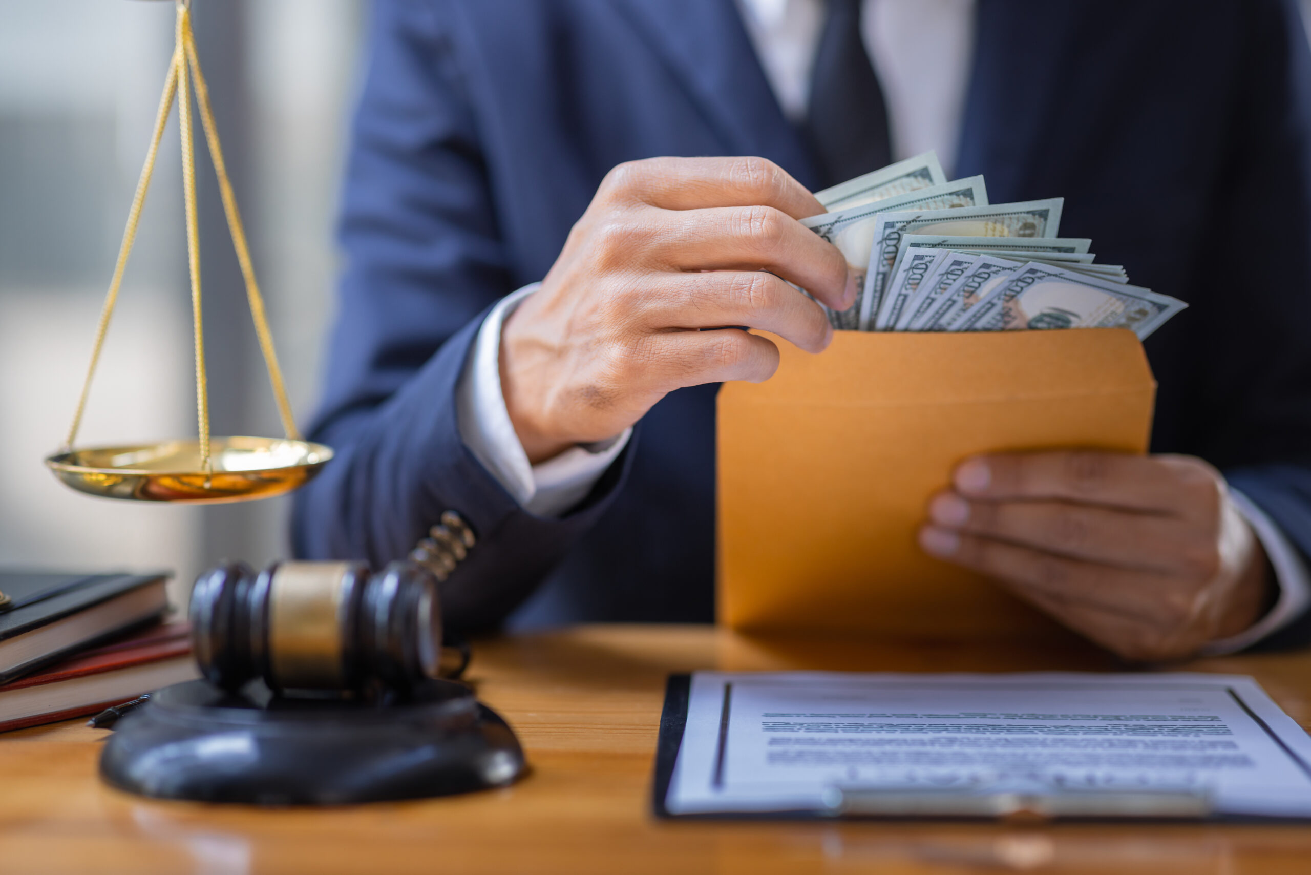 Close-up of a professional handling legal documents and money beside a gavel and scale, symbolizing the need for neutral, confidential, and legally informed oversight in workplace investigations.