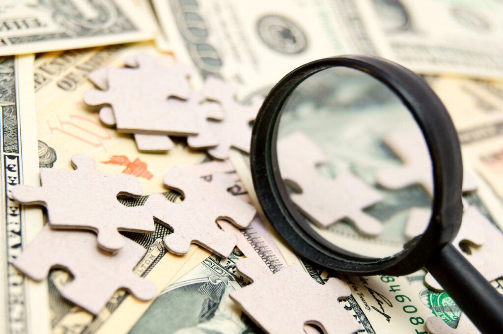 Magnifying glass over puzzle pieces and dollar bills, symbolizing the hidden financial and cultural costs of promoting untrained managers.