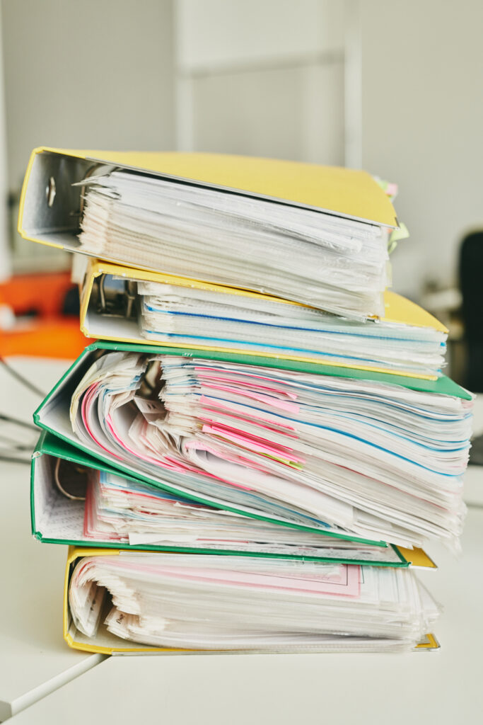 Stack of overloaded binders filled with paperwork, symbolizing the risks of outdated or generic employee handbooks with inconsistent or incomplete policies.
