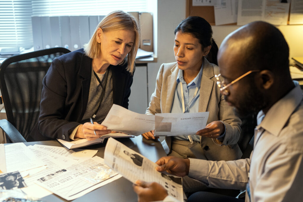 Three professionals reviewing HR documents together, symbolizing a systematic HR compliance audit that evaluates policies, procedures, employee files, and wage and hour practices.